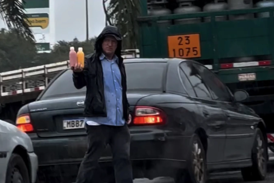 João vendendo sucos à beira de uma estrada, em frente a carros